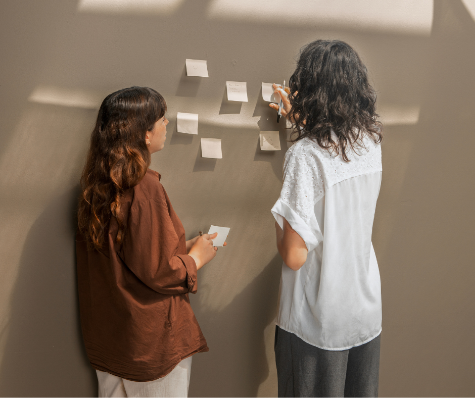 Zdjęcie przedstawia dwie kobiety przyklejające kartki z notatkami na ścianę.