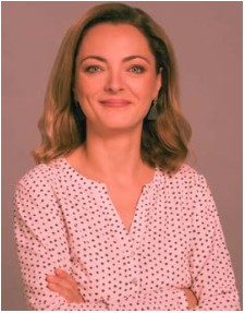 Zdjęcie przedstawia uśmiechniętą blondwłosą kobietę we wzorzystej koszuli.