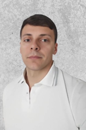 Zdjęcie przedstawia młodego mężczyznę z krótkimi ciemnymi włosami, ubranego w białą koszulę.