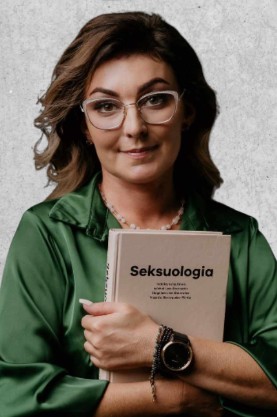 Zdjęcie przedstawia kobietę z brązowymi włosami i okularami. Ubrana w zieloną koszulę trzyma książkę zatytułowaną "Seksuologia"