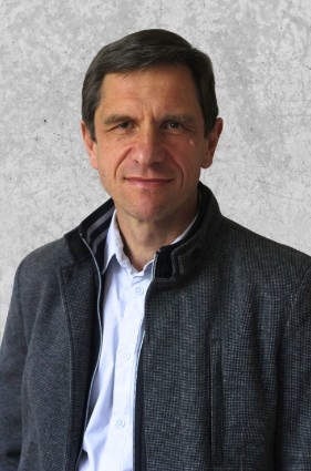 Zdjęcie przedstawia mężczyznę o krótkich czarnych włosach. Ubrany w koszulę i rozpięty polar.