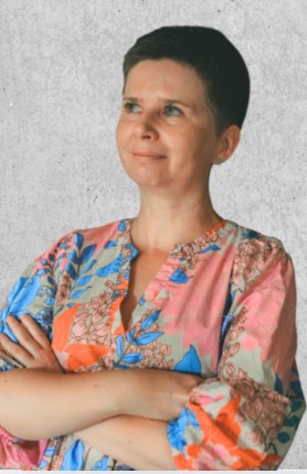 Zdjęcie przedstawia kobietę z krótkimi, ciemnymi włosami, ubraną w wzorzystą koszulę.
